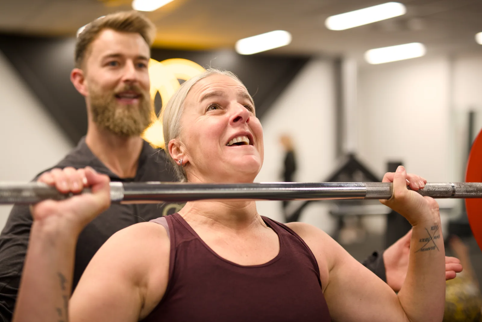 A member practising a barbell press with guidance from an OC coach
