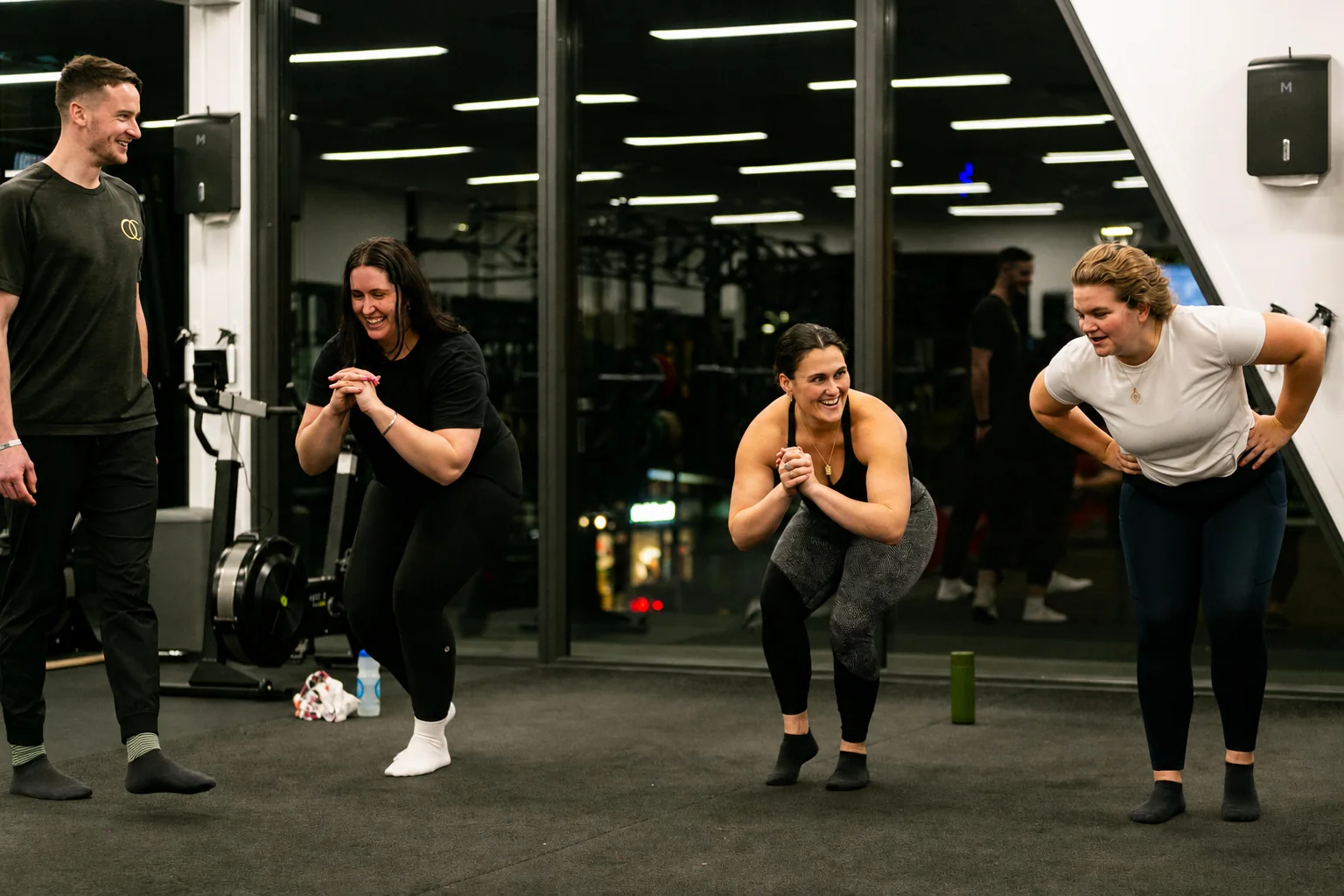 An OC coach guiding members through a squat in a group class